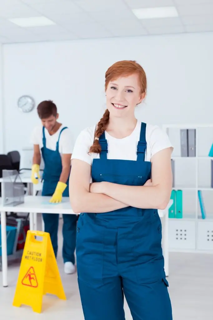 Smiling female cleaners folding hands. at the back the a male cleaner cleaning desk