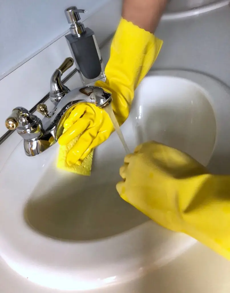 Woman cleaning the sink in the bathroom while doing home chores.