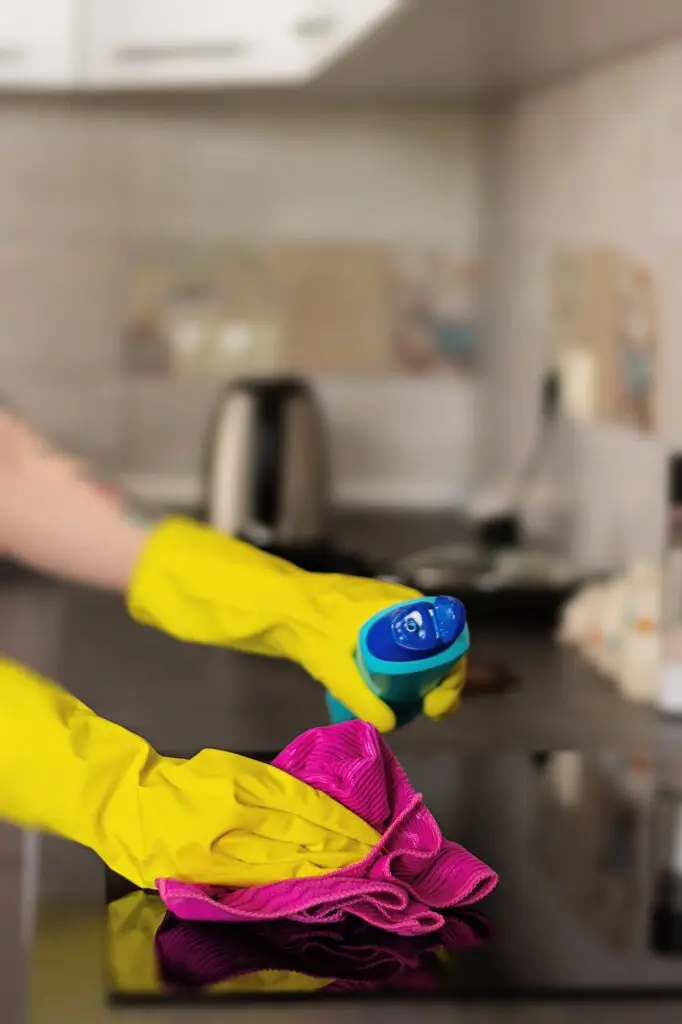 Woman in protective gloves wiping dust using cleaning spray and duster. Cleaning service concept.